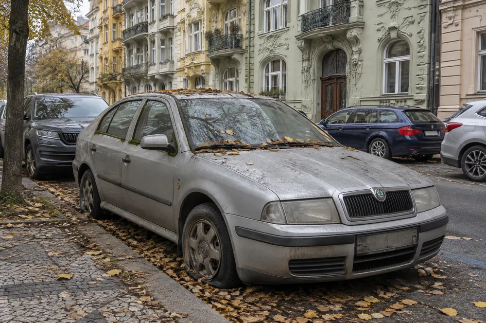 Zaprášená stříbrná Škoda Octavia s prázdnou pneumatikou stojí dlouho u chodníku mezi secesními domy na Vinohradech